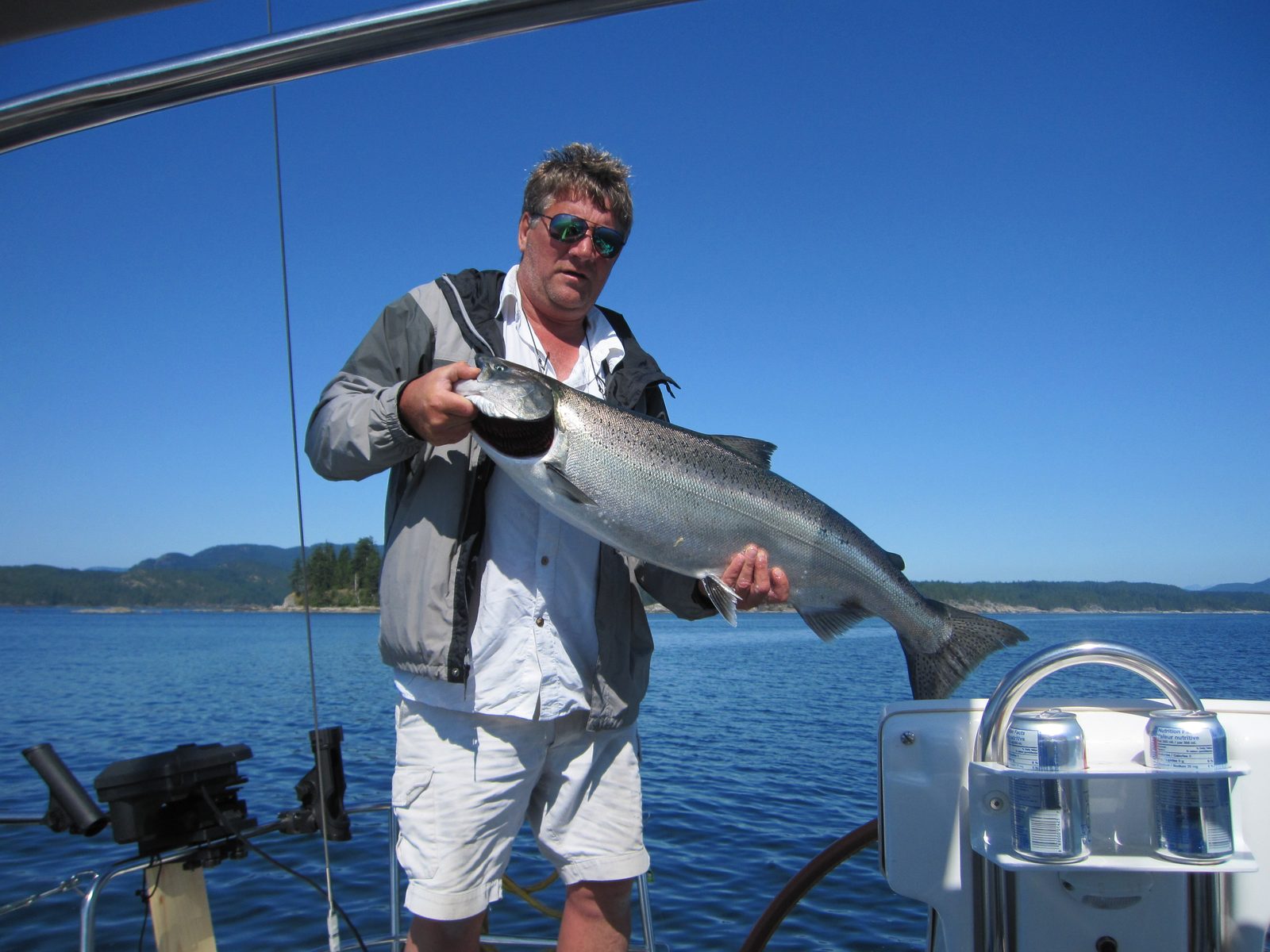 Todd holding a chinook salmon on the boat, sunglasses and blue sky
